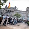 Menschen stehen am Reichstagsgebäude des Deutschen Bundestages vor der Besucherkontrolle.
