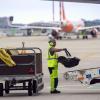 Ein Flughafen-Mitarbeiter lädt auf dem Vorfeld des Flughafens BER einen Kindersitz auf das Gepäck-Transportband am Flugzeug.