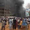 Mit dem brennenden Hauptquartier der Regierungspartei im Rücken demonstrieren Anhänger meuternder Soldaten in der Hauptstadt Niamey.