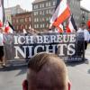 Vor dem Zug der Neonazi-Demonstration anlässlich des 31. Todestages von Rudolf Heß kniet ein Mann mit einer Fisur, die bei Neonazis üblich ist.