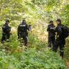 Polizisten durchsuchen ein Waldstück, in dessen Nähe eine weibliche Leiche in einem PKW entdeckt wurde.