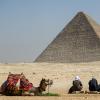 Ein Kamel und seine Reiter rasten vor der Großen Pyramide von Gizeh.