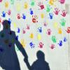 Ein Mann mit zwei Kindern wirft einen Schatten auf eine bemalte Wand einer Kindertagesstätte.