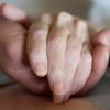 Ein Pfleger hält die Hand einer alten, kranken Frau, die als Pflegefall bettlägerig ist. Das heißt aber nicht, dass sie sterben will.  