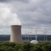 Dampf steigt aus den Kühltürmen eines Atomkraftwerks. Im Hintergrund sind Windräder zu sehen.