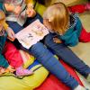 Eine Erzieherin in einer Kindertagesstätte liest zwei Mädchen aus einem Buch vor.