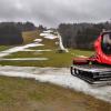 Eine Pistenraupe steht auf einer Skipiste, die nur noch teilweise mit Schneeresten bedeckt ist.