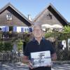 Grafiker Alfred Beschle mit der Chronik vor dem „Sirch“-Haus in Utting mit der neuen Uttinger Chronik, die heute der Öffentlichkeit vorgestellt wird.  