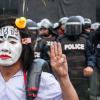 Ein geschminkter Teilnehmer einer regierungskritischen Demonstration hebt als Zeichen des Widerstands vor einer Polizeiabsperrung die Hand zum drei-Finger-Gruß.  