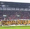 14. Mai 2016. Letztes Saisonspiel des FC Augsburg gegen den Hamburger SV. Nach dem Schlusspfiff trägt die komplette FCA-Mannschaft ein Plakat mit der Aufschrift „Simon, du wirst siegen!“ durch die Arena. 
