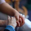 Eine junge Frau hält in einem Pflegeheim die Hand einer Seniorin.