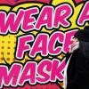 Eine Frau ohne Mund-Nasen-Schutz geht an einem farbigen Schild in Nottingham vorbei, das zum Tragen einer Mund-Nasen-Bedeckung auffordert.