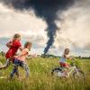 Begleitet von zwei Freundinnen lernt die fünfjährige Alina in der Ukraine Fahrradfahren, während im Hintergrund eine dunkle Wolke zu sehen ist. In der Nacht zuvor hat eine russische Drone ein Öllager in Brand gesetzt.