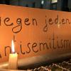 Eine brennende Kerze steht vor einem Schild mit der Aufschrift "Gegen jeden Antisemitismus".