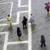 Touristen waten in Regenkleidung über den Markusplatz. Venedig wird wegen seiner Lage in der Lagune immer wieder von Hochwasser heimgesucht, die Lage verschärft sich aber zunehmend.