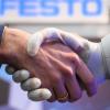An einem Stand der Unternehmensgruppe für Steuerungs- und Automatisierungstechnik Festo gibt ein Roboter einem Mann die Hand. 
