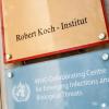 Ein Schild mit der Aufschrift "Robert Koch-Institut" weist auf den Eingang des Gebäudes hin.