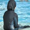 Eine muslimische Schülerin sitzt  in einem Ganzkörper-Badeanzug am Rande des Schwimmbeckens.