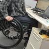 Ein Mann sitzt in einem Rollstuhl an seinem Arbeitsplatz am Schreibtisch. Immer wieder hilft die Kartei der Not auch Schwerbehinderten. 