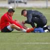 Raul Bobadilla FC Augsburg sitzt auf dem Rasen und wird von Physiotherapeut Michael Deiss  an der Wade bandagiert.