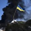 Eine ukrainische Flagge weht auf einem Kontrollpunkt, während schwarzer Rauch aus einem Treibstofflager der ukrainischen Armee nach einem russischen Angriff aufsteigt.