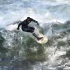 Ein Surfer surft auf der Eisbachwelle im Englischen Garten bei schönstem Frühlingswetter.