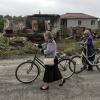 Zwei Frauen gehen mit ihren Fahrrädern auf einer Straße neben zerstörten russischen Schützenpanzern und zerstörten Häusern spazieren.