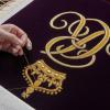Ein Mitglied der Royal School of Needlework stickt den Schriftzug von Queen Camilla von Hand auf deren Robe.