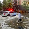 Hochwasser auf den Straßen von New York: Im Stadtteil Brooklyn versucht ein Mann, mit einem Stock einen Abfluss zu reinigen, während ein Polizeiwagen vorbeifährt.