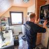 Ein Mitarbeiter einer Sanitär- und Heizungsbaufirma installiert eine moderne Gasbrennwerttherme in einem Einfamilienhaus.