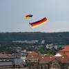 Ein Fallschirmspringer über Dresden zieht eine Deutschlandfahne hinter sich her.