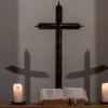 Kerzen, eine Bibel, ein Kreuz und die Schatten des Kreuzes sind in einer Kapelle zu sehen.