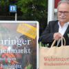 Bürgermeister Manfred Nerlinger lädt mit einer neuen Tasche zum Einkauf auf dem Wehringer Wochenmarkt ein.  