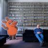 Armin Maiwald, Filmemacher, Autor und Miterfinder der Sendung mit der Maus sitzt auf einem Sofa in seinem Büro vor zahlreichen Filmrollen. 