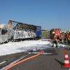 Einsatzkräfte der Feuerwehr richten einen Schlauch auf einen ausgebrannten Lastwagen.