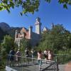 Touristen stehen auf einer Aussichtsplattform vor dem Schloss Neuschwanstein.