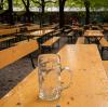 Ein leerer Bierkrug an einer leeren Bierbank eines leeren Biergartens.