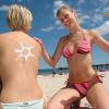 Mit Sonnencreme reibt Sandy ihre Freundin Katja am Strand des Seebades Binz auf der Insel Rügen ein.