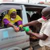 Ein Arbeiter desinfiziert die Hände einer Frau auf einem Sammelpunkt für Taxis.  In Uganda steigen derzeit die Corona-Zahlen.