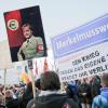 Ein Pegida-Anhänger zeigt ein Plakat, auf dem Merkel in Nazi-Uniform zu sehen ist.