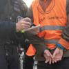 Ein Aktivist der Klimaschutz-Gruppe Letzte Generation steht in Handschellen neben einem Polizeibeamten.