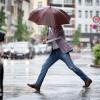 Ein Mann läuft in Düsseldorf im strömenden Regen mit einem Schirm über eine Straße. Auch in Bayern herrscht derzeit herbstliche Stimmung.