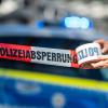 Ein Absperrband wird vor einem Polizeiwagen ausgerollt.