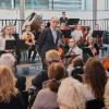 Schulleiter Karl Höldrich bei seiner Begrüßungsrede zur Einweihung der neuen Übungsräume in der Mozartvilla. Im Hintergrund das Schüler- und Jugendorchester der Musikschule Augsburg, das für den musikalischen Rahmen sorgte. 	