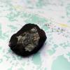 Das 508 Gramm schwere Stück eines Meteoriten stürzte am 15. Februar bei Tscheljabinsk ab. Dunkel ist die Schmelzkruste, das helle Teil ist das „Fenster“. Im Hintergrund eine Karte, auf der Karl Wimmer die Flugkurve der Steine erfasst hat. Im Fallen wurde der Stein vom Wind abgelenkt, deswegen machte er scheinbar einen Haken. 
