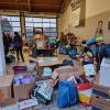 Freiwillige stehen in der vollgestellten Bauhofhalle und sortieren die Waren. Tatkräftig werden sie auch von Sielenbacher Kindern  unterstützt.