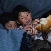 Zwei Kinder, die  aus der Türkei auf die griechische Insel Lesbos gekommen sind, liegen im Dorf zusammen unter einer Decke und essen Fladenbrot.