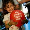 Ein kleines Mädchen aus Syrien hält in München nach der Ankunft mit einem Zug aus der ungarischen Hauptstadt am Hauptbahnhof diesen roten Ballon.