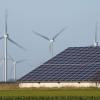 Windenergieanlagen stehen neben einer Halle mit Photovoltaik-Anlagen.