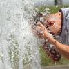 Bei Temperaturen um 29 Grad Celsius erfrischt sich ein junger Mann am Wasser eines Brunnens.